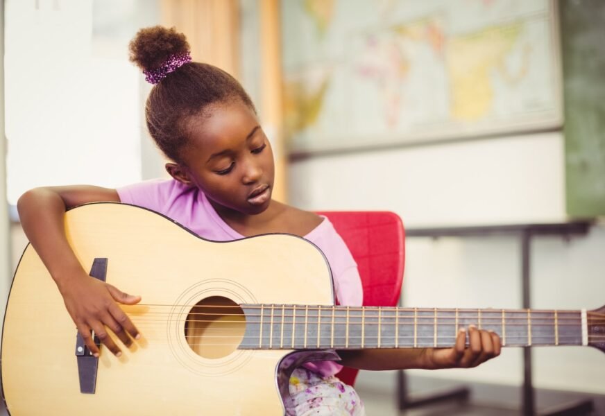 Close,Up,Of,Schoolgirl,Playing,Guitar,In,Classroom,At,School